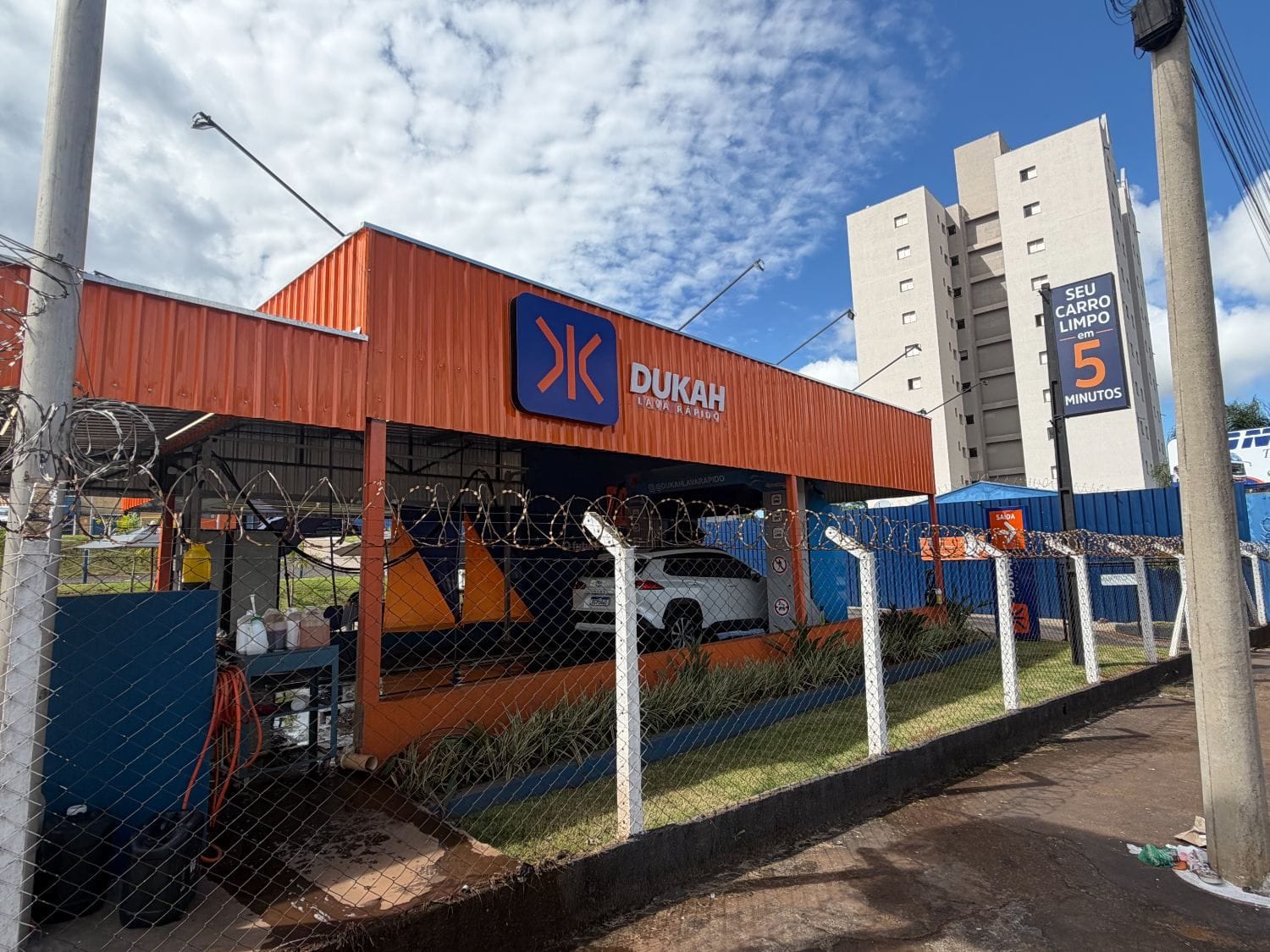 Lateral da fachada Dukah com cerca e totem 5 minutos visível