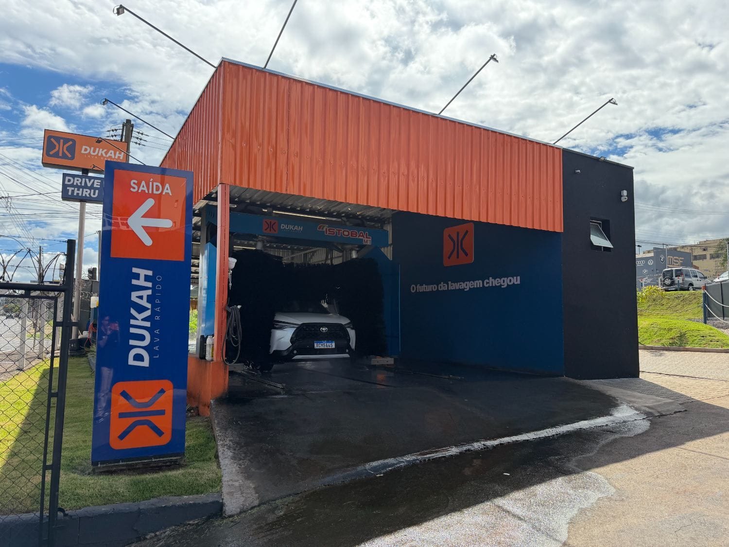 Saída do drive thru com placa SAÍDA e Corolla saindo do bay